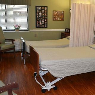 A hospital room with two beds separated by a curtain, featuring chairs and a wooden floor.