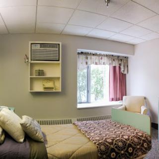 A comfortable hospital room featuring a bed, an air conditioning unit, and a cozy sitting area by the window.