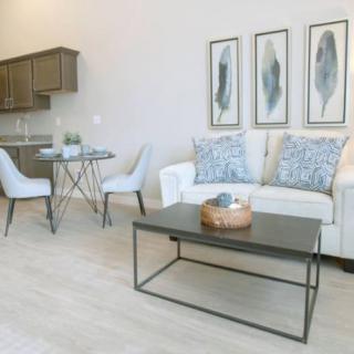 A modern, minimalist living room with a sofa and coffee table, featuring decorative artwork and an adjacent dining area.