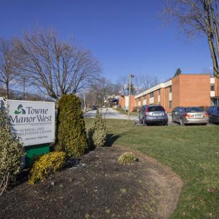 A view of the Town Manor West property featuring a sign and well-maintained landscaping.