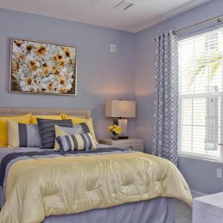 A cozy bedroom featuring a neatly made bed with yellow and gray bedding, complemented by a stylish lamp and artwork on the wall.
