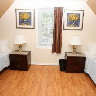 A cozy bedroom with twin beds, nightstands, and lamps on a hardwood floor.