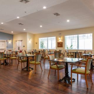 An elegant dining area with neatly arranged tables and chairs, featuring wooden flooring and ample natural light.