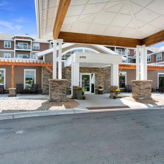A modern building entrance featuring a covered driveway with stone pillars and large windows.
