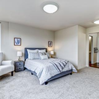 A modern bedroom with a neatly made bed, white armchair, and stylish decor.