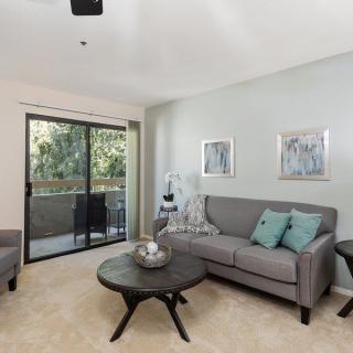 A modern living room with a comfortable sofa and coffee table, featuring minimalist decor and abundant natural light through a sliding glass door.