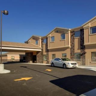 A hotel building with a parking lot and a white car in front on a sunny day.