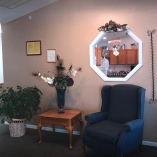 A cozy living room with a blue armchair, decorative mirror, and a wooden table with a plant.