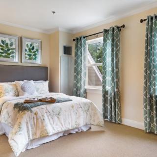A cozy bedroom featuring elegant curtains, a comfortable bed, and framed artwork on the walls.