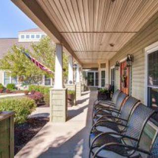 A sunlit porch with a row of chairs overlooking a garden and well-maintained landscaping.
