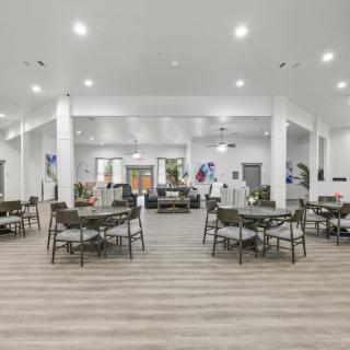 A spacious and modern dining area with tables and chairs arranged under bright lighting on wooden flooring.