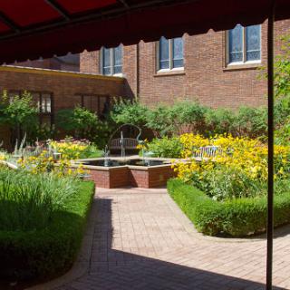 A serene garden featuring a fountain surrounded by vibrant flowers and neatly manicured hedges.