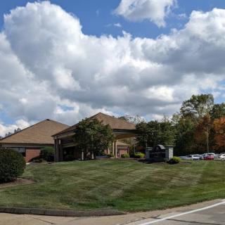 A picturesque scene featuring a building surrounded by lush grass and beautiful clouds in the sky.