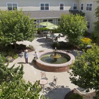 A peaceful courtyard featuring a central fountain surrounded by trees, tables, and chairs.