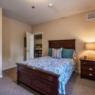 A cozy bedroom with a wooden bed frame, decorative pillows, and a nightstand with a lamp.