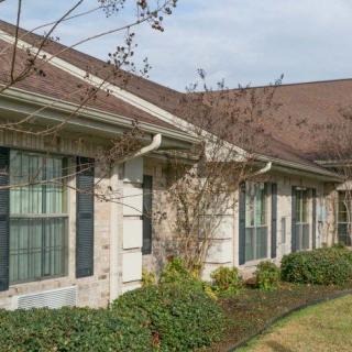 A residential building with a brown roof, white brick exterior, and landscaped surroundings.