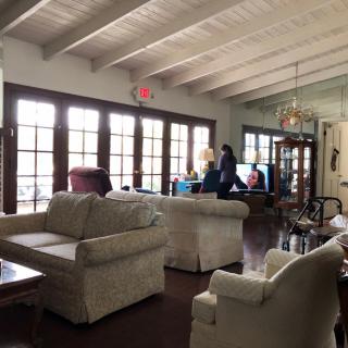 Spacious living room with comfortable seating, large windows, and people interacting at a table.