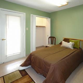 A minimalist bedroom with green walls, featuring a single bed and an open closet.