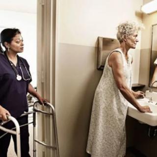 A nurse assists an elderly woman using a walker in the bathroom.