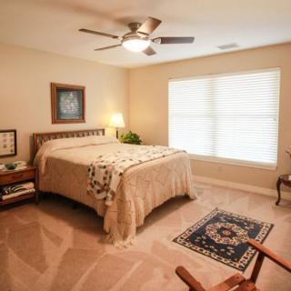 A cozy bedroom with a neatly made bed, carpeted floor, and warm lighting.