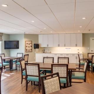 A modern community dining room with tables, chairs, and a kitchenette.