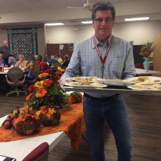 A person carrying a tray of food at a festive event with autumn-themed decorations.