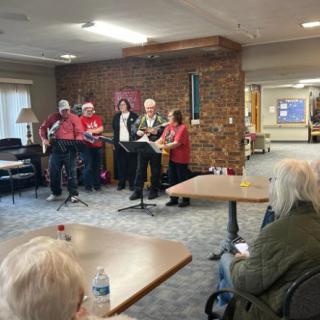 A group of musicians performs for seniors in a cozy indoor setting.