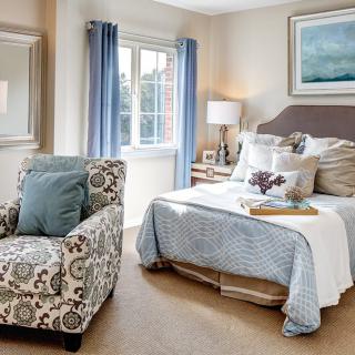 A cozy and stylish bedroom with a patterned armchair, comfortable bed, and soft lighting.