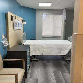 A modern hospital patient room featuring a clean bed and comfortable seating.