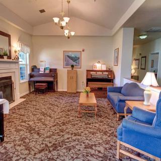 A cozy living room featuring a fireplace, blue sofas, a patterned carpet, and a piano.
