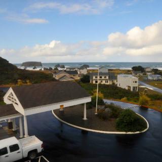 A scenic view of a coastal town with the ocean in the background, surrounded by buildings and a parking area under a partly cloudy sky.
