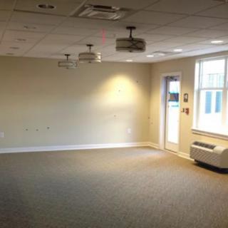 An empty room with carpet flooring and natural light coming through windows.
