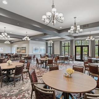 A spacious and elegant dining room with round tables, upholstered chairs, and multiple chandeliers.