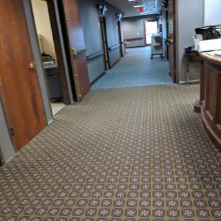A view of an office hallway featuring carpet, doors, and a reception area.