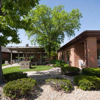 A peaceful outdoor setting with landscaped gardens and brick buildings under a clear blue sky.