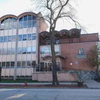 A modern commercial building with a mix of glass and brick architecture, featuring large windows and surrounded by greenery.