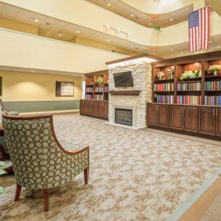 A spacious lobby with a fireplace, bookshelves, and seating area under an atrium with an American flag.