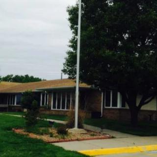 A low-rise building with a flagpole in front, surrounded by trees and a sidewalk.