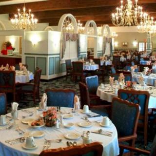 An elegant restaurant dining room with chandeliers, set tables, and upholstered chairs.