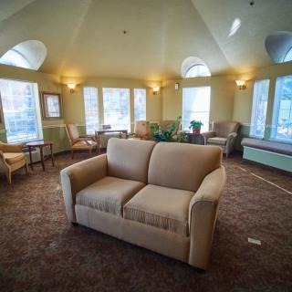 A cozy living room with a central sofa, carpeted floor, and large windows providing ample natural light.
