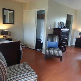 A cozy bedroom with modern furniture, featuring a striped chair, dresser, and hardwood flooring.