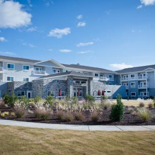 A large residential building with a landscaped garden under a blue sky.