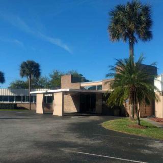 A building with palm trees and a driveway under a clear blue sky.