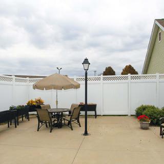 A tidy outdoor patio area featuring a seating arrangement with an umbrella, surrounded by a white fence and adorned with potted plants.