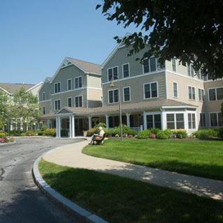 A large residential building with a well-maintained lawn and surrounding greenery on a sunny day.