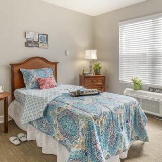 A cozy, well-lit bedroom with a single bed adorned with a colorful quilt and matching pillows.