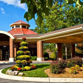 A beautifully landscaped entrance with a circular driveway and a well-maintained garden in front of a brick building.