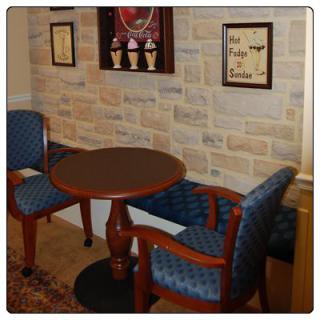 A cozy seating area with a round wooden table and two upholstered chairs, set against a decorative brick wall adorned with framed artwork.