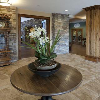 A stylish lobby interior featuring a wooden table with an orchid centerpiece, surrounded by stone walls and warm decor.