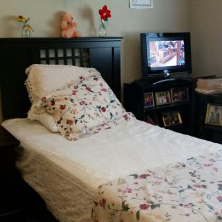 A cozy bedroom with a bed featuring floral bedding and a TV on a shelf.